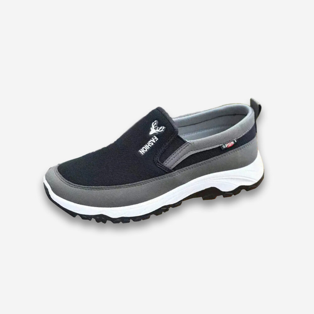 Une basket orthopédique homme décontractée de couleur noire, grise et blanche, sans lacet, sur un fond gris très clair uni.