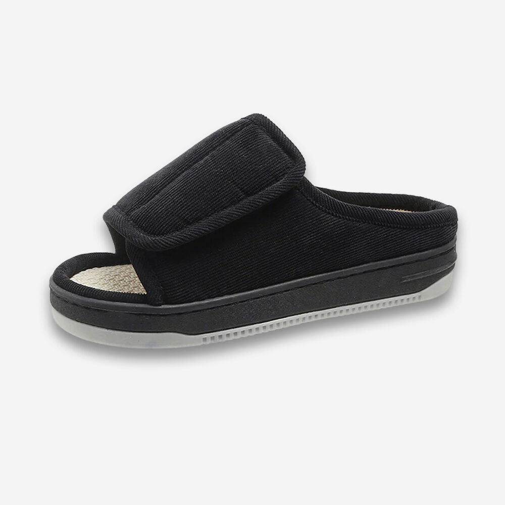 Un chausson orthopédique pour homme à bout ouvert façon claquette, de couleur noire, sur un fond gris très clair uni.