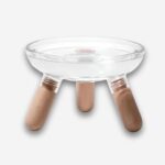 Bol orthopédique pour chat avec coupelle transparente. 3 pieds de couleur bois clair. Sur fond uni clair.