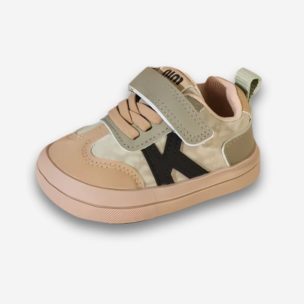 Chaussures orthopédiques enfant style sneakers de couleurs beige et kaki avec un scratch et de faux lacets. La lettre K sur le côté. Sur fond uni clair.