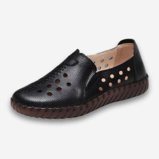 Chaussures orthopédiques femme en similicuir souple de couleur noire. Le similicuir est perforé sur l'ensemble de la chaussure. Le semelle en caoutchouc est marron. Sur fond uni clair.