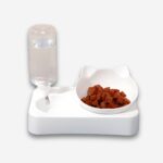 Gamelle orthopédique pour chat avec distributeur d'eau en plastique blanc. Le bol à droite a des oreilles de chat et de la nourriture à l'intérieur. Sur fond uni clair.