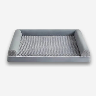 Lit orthopédique pour chien avec rebords de couleur grise. De forme rectangulaire avec trois rebords et une surface pelucheuse. Sur fond uni clair.