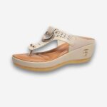 Sandales orthopédiques compensées pour femme beige avec détails dorés sur le dessus, ouvertes comme une tong avec le talon plus épais. Sur fond uni clair.