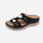 Sandales orthopédiques fleuries en similicuir pour femme de couleur noire avec talon compensé. Sur fond uni clair.