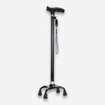 Une canne marche orthopédique antidéparante à base large, entièrement noire avec un corps en aluminium et 4 pieds antidérapants écartés, vue de profil sur un fond gris très clair uni.