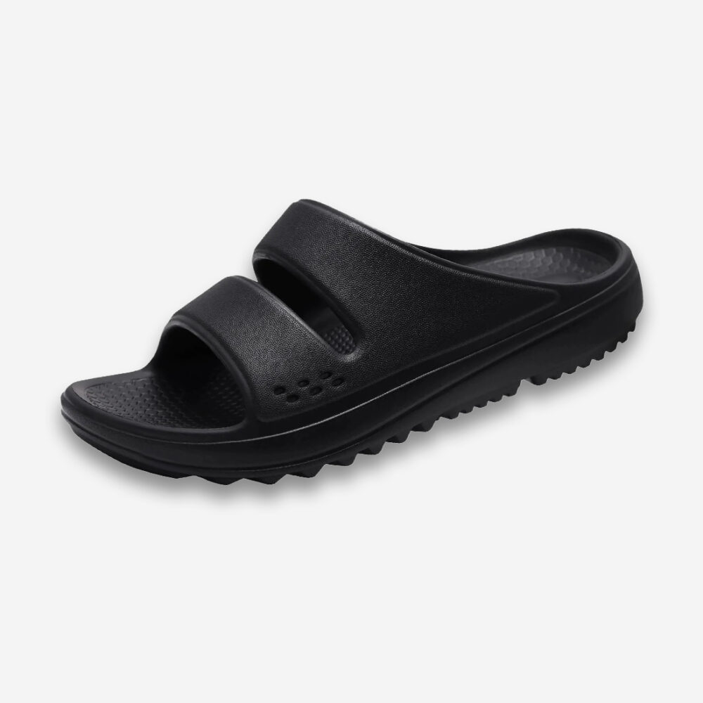 Une claquette orthopédique pour homme super souple en mousse et à semelle crantée, de couleur noire, disposée sur un fond gris très clair uni.