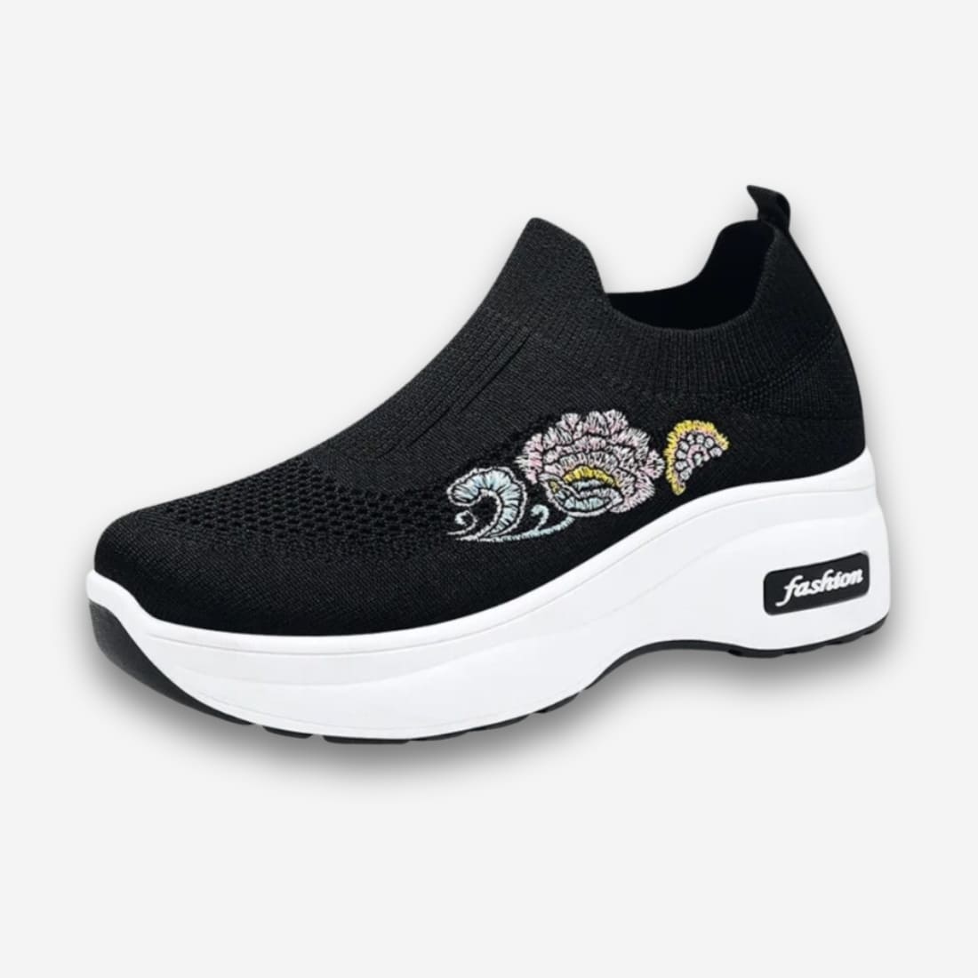 Baskets orthopédiques pour femme avec fleur brodée. La chaussure est en tissu respirant noir sans lacets. Sur fond uni clair.
