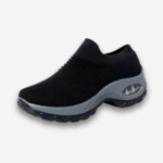 Baskets orthopédiques sans lacets pour femme de couleur noir avec une semelle gris foncé. Sur fond uni clair.