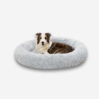 Chien couché dans un panier rond en fausse fourrure grise avec rebords surélevés, sur fond neutre.