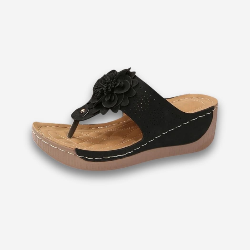 Tongs orthopédiques fleuries à plateforme pour femme de couleur noire avec la semelle beige. Sur fond uni clair.