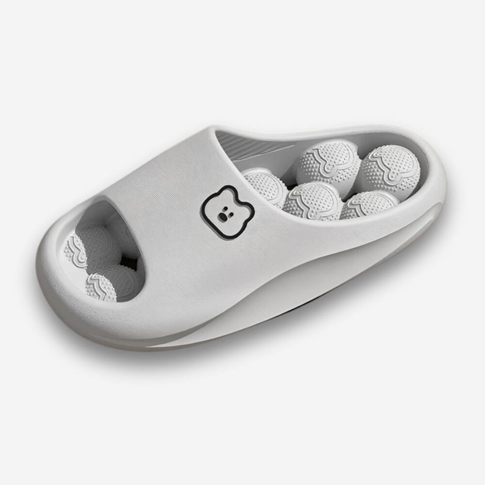 Claquettes orthopédiques massantes pour femme de couleur grise avec des boules à picots sur l'intérieur de la semelle en EVA. Une tête d'ours sur la bande large. Sur fond gris très clair.
