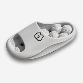 Claquettes orthopédiques massantes pour femme de couleur grise avec des boules à picots sur l'intérieur de la semelle en EVA. Une tête d'ours sur la bande large. Sur fond gris très clair.