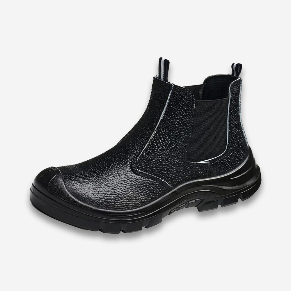 Une chaussure de sécurité orthopédique style bottine Chelsea entièrement noire avec enfilage facilité par une bande élastique latérale, sur un fond gris très clair uni.