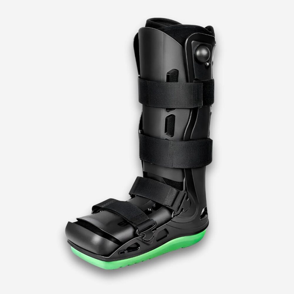 Bottes orthopédiques à coque intégrale de couleur noire et rigide. Le dessous est vert fluo. Quatre sangles ajustables noires. Sur fond uni clair.