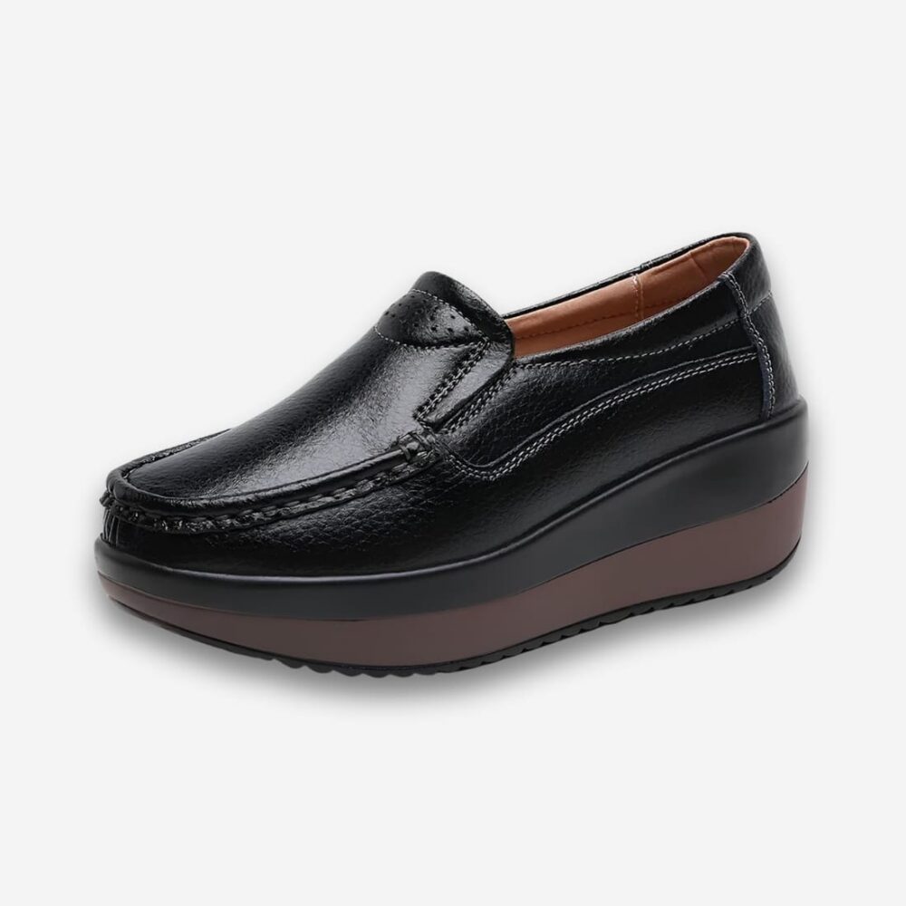 Chaussures orthopédiques style mocassins pour femme en similicuir de couleur noire avec une semelle épaisse. Sur fond uni clair.
