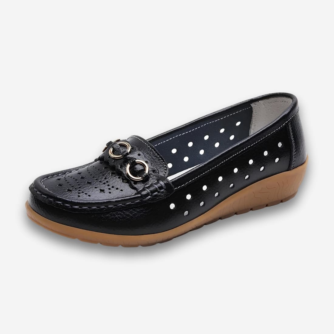 Chaussures orthopédiques style mocassins vintage pour femme de couleur noire avec des détails dorés sur l'avant. Le cuir synthétique est perforé et la semelle marron en caoutchouc. Sur fond gris très clair.