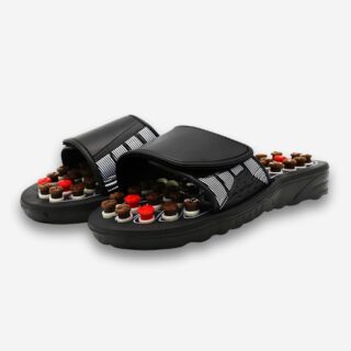 Claquettes orthopédiques avec points d'acupression pour femme. Les claquettes sont noires, les points d'acupression sur la semelle sont marron et rouge. Sur fond gris très clair.