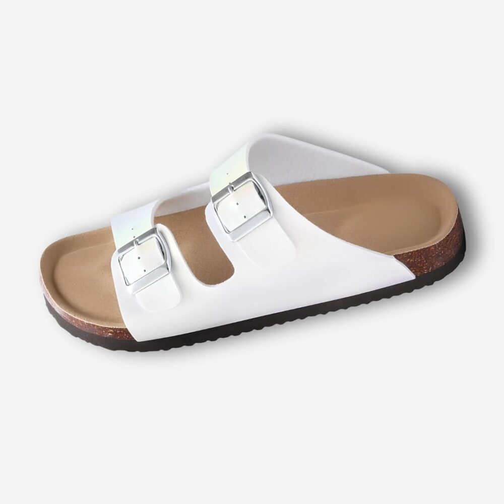 Mules orthopédiques pour femme coloris irisés. Vue de profil, une mule blanche à deux brides avec boucle. La semelle intérieure est de couleur liège. Sur fond uni clair.