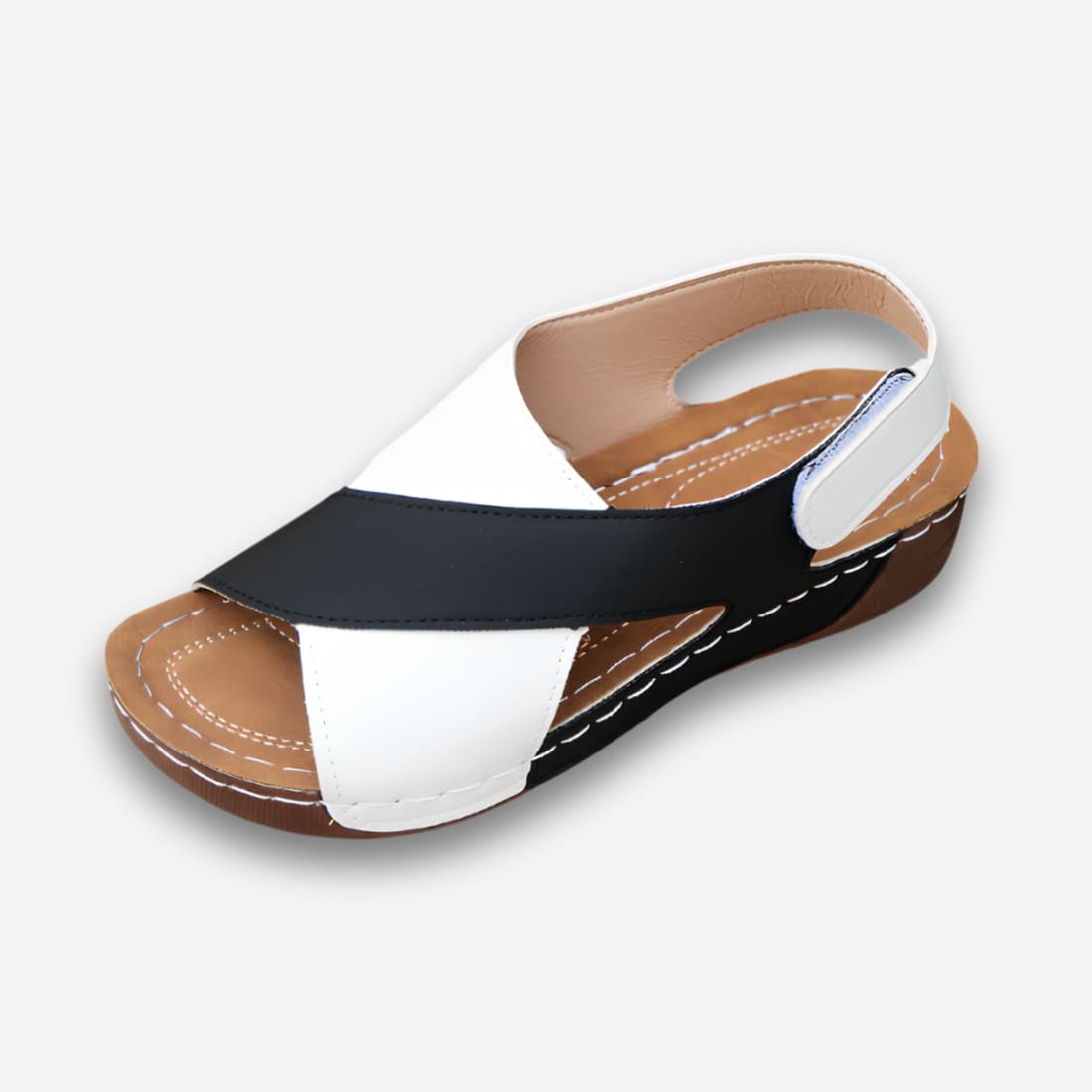 Sandales orthopédiques élégantes et ajustables pour femme avec une semelle légèrement compensées, une bride à l'arrière avec un scratch. Le design de devant est formé de deux parties : une blanche et une noir qui se croisent. Sur fond uni clair.