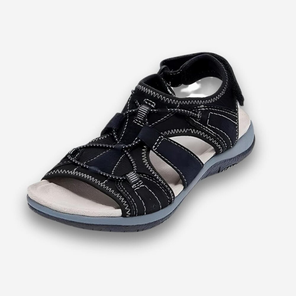 Sandales orthopédiques plates pour femme de couleur noire avec une semelle amortissante et un scratch à l'arrière de la chaussure. Sur fond uni clair.