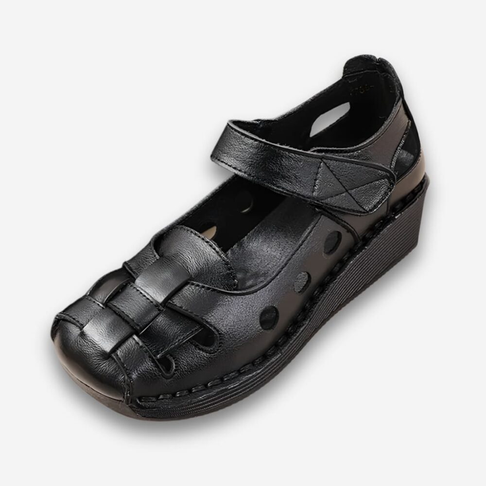 Sandales orthopédiques vintage à bout rond pour femme de couleur noire avec bride à la cheville et similicuir ajouré. Sur fond uni clair.