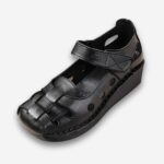 Sandales orthopédiques vintage à bout rond pour femme de couleur noire avec bride à la cheville et similicuir ajouré. Sur fond uni clair.