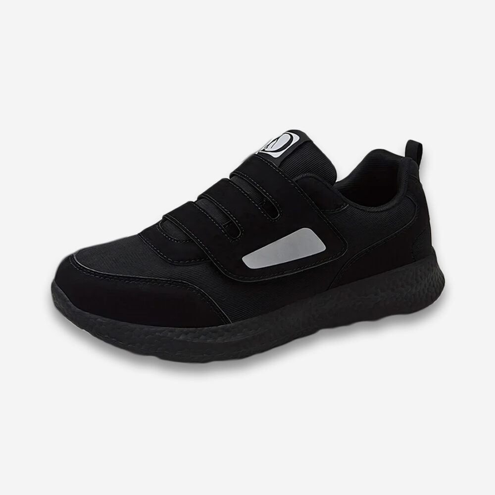 Une basket orthopédique homme pour pied enflé à scratch et ouverture facile, entièrement noire avec une pointe de gris sur la languette, vue de profil sur un fond gris très clair uni.
