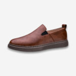 Une chaussure orthopédique homme mocassins rembourré de couleur marron, dans un cuir patiné, de profil sur un fond gris très clair uni.