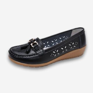 Chaussures orthopédiques mocassins à gland en cuir ajouré pour femme de couleur noire avec une semelle marron en caoutchouc. Sur fond gris très clair.