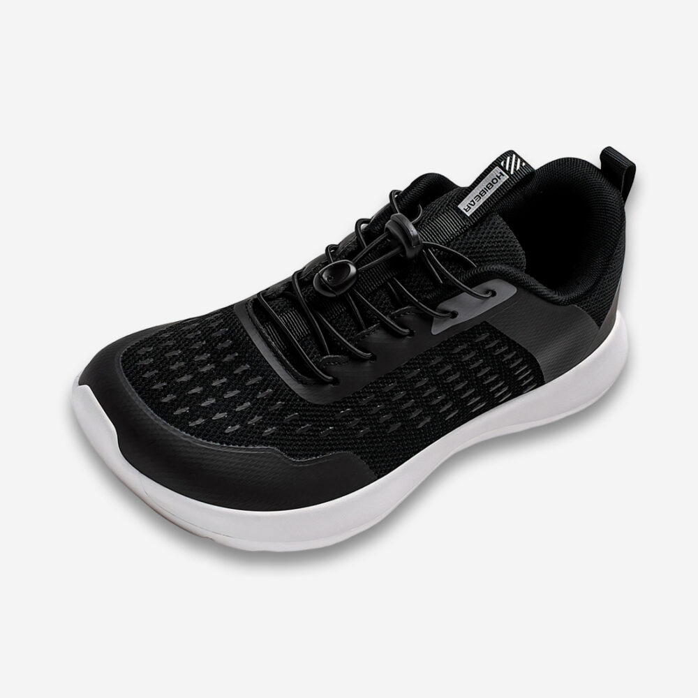 Une basket orthopédique homme à bout large pour running noire à la semelle blanche avec des lacets noirs en élastique, vue de 3/4 sur un fond gris très clair uni.