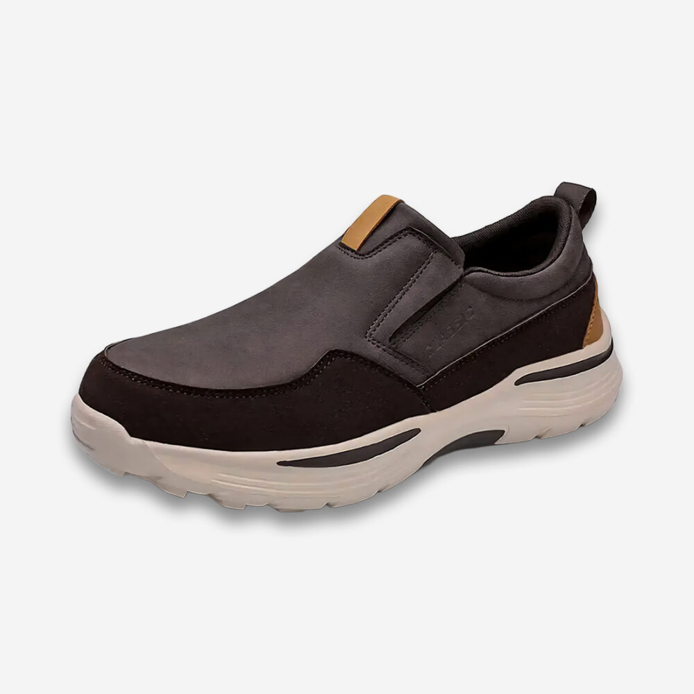 Une basket orthopédique homme en cuir vegan marron foncé avec des renforcements encore plus foncés et une semelle couleur crème, de 3/4 sur un fond gris très clair uni.