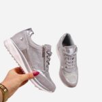 Paire de baskets compensées grises avec des strass, confort orthopédique. L'une est tenue dans la main d'une femme de profil, et l'autre chaussure est de face vue d'en haut.